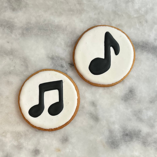 Two cookies with black music note designs on white icing, placed on a marble surface.